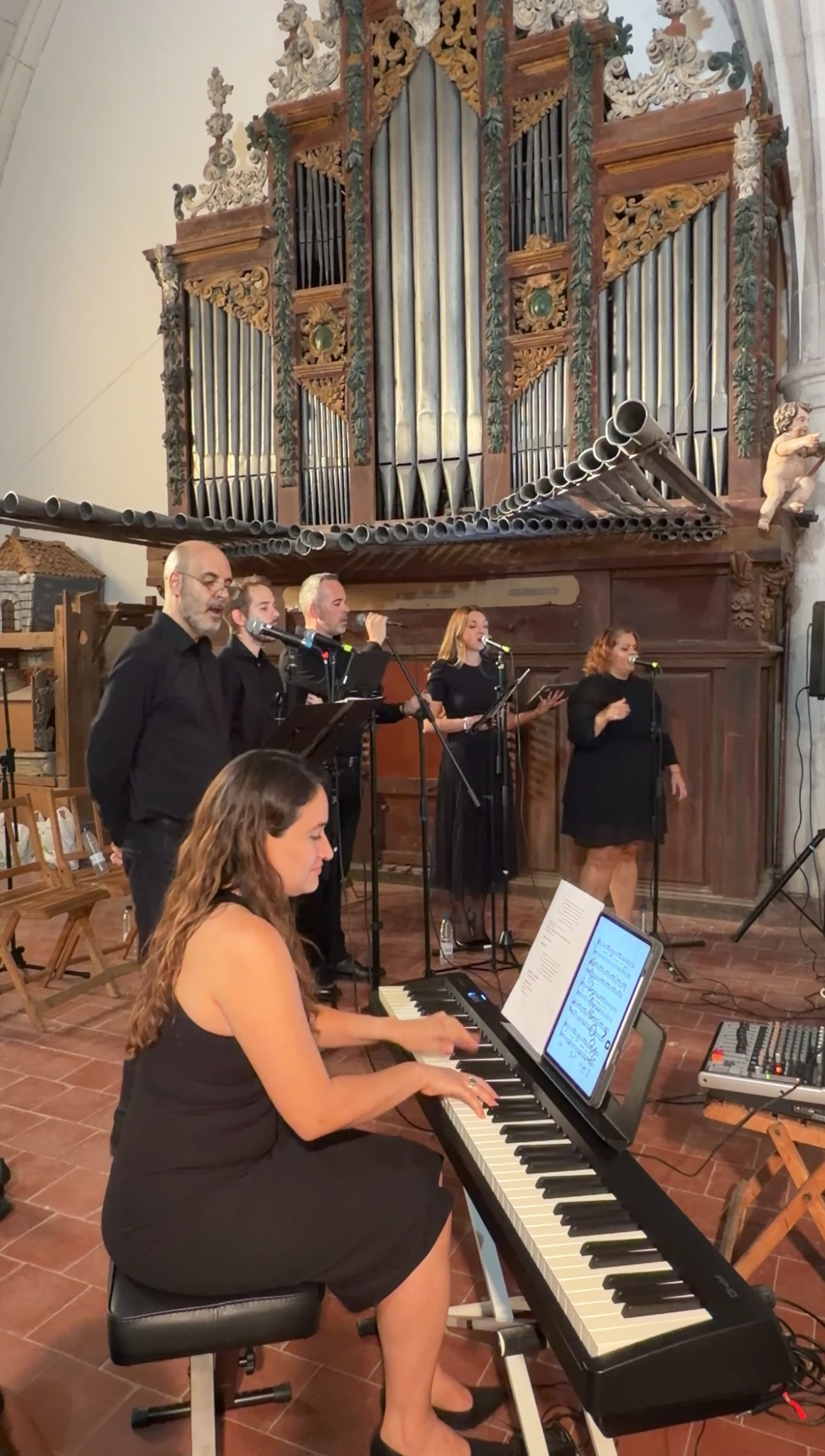 Cinco cantantes actuando junto a una pianista ante un órgano de iglesia